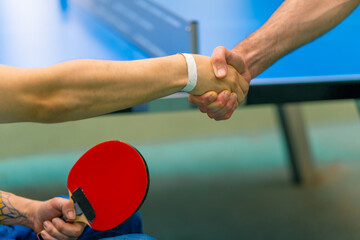 An inclusive disabled man with a racquet in his hand shakes hands with an older man before a game...