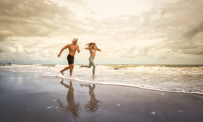Sport man and woman running on beach at sunset. Summer concept
