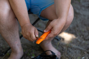 A man cleans carrots with a knife, preparing vegetables