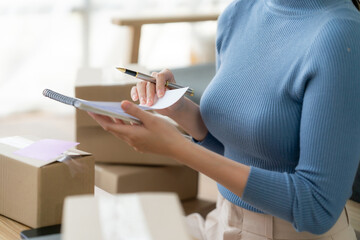 Young business owner woman prepare parcel box and standing check online orders for deliver to customer on tablet, laptop Shopping Online concept.