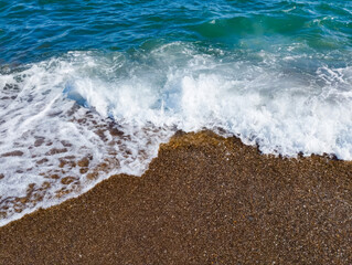 Beautiful sea background with pebble beach and blue waves with sea foam.
