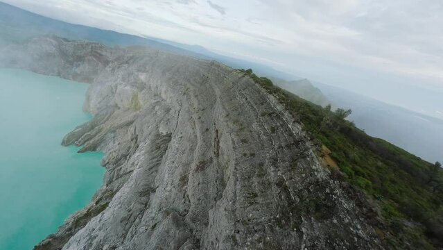 Volcano crater with acidic turquoise lake strolling tourists on edge of cliff aerial view. FPV sport drone captures dynamic footage majestic mountain landscape mountain range breathtaking scenery 4k