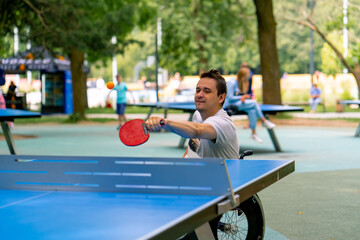 Inclusiveness A disabled man in a wheelchair plays ping pong in a city park against a backdrop of...
