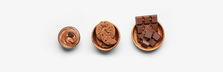 Bowls with tasty cookies, chocolate and cream on light background