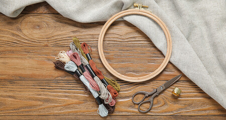 Embroidery hoops with threads, scissors, thimble and canvas on wooden background © Pixel-Shot