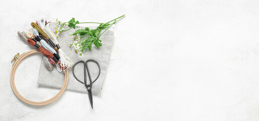 Wooden embroidery hoops with threads, scissors, chamomile flowers and canvas on light background with space for text © Pixel-Shot
