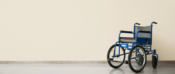Fototapeta na wymiar Empty wheelchair near light wall with space for text