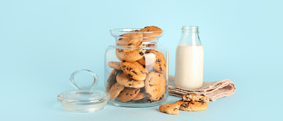 Jar with tasty cookies and bottle of milk on light blue background