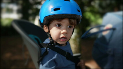 Child wearing helmet in bicycle back seat riding bike with parent