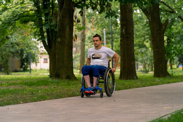 Inclusiveness A man with disabilities rides a wheelchair along the path of a city park against the...