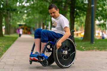 Inclusiveness A man with disabilities rides a wheelchair along the path of a city park against the...