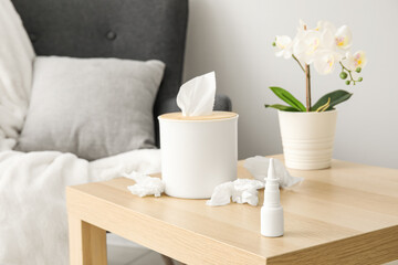 Fototapeta na wymiar Nasal drops with tissue box on table in living room, closeup. Allergy concept