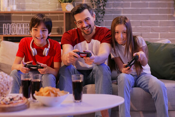 Father with his little children playing video game at home in evening