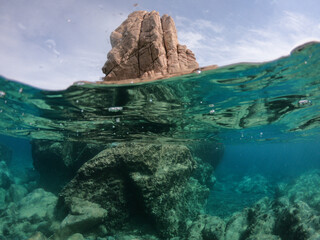 half under water view of the sea shore near a beach in sardinia italy with turquoise water, rocks and blue sky
