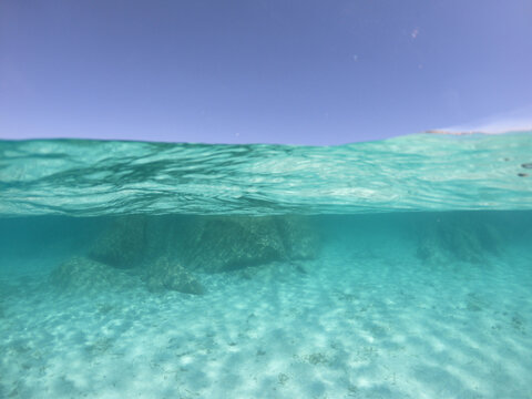 half under water view of the sea shore near a beach in sardinia italy with turquoise water, rocks and blue sky