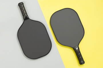 Close top view of two black pickleball paddles on yellow and gray diagonal background. Sport game...
