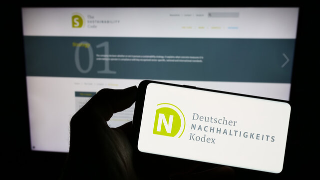 Stuttgart, Germany - 07-11-2023: Person holding cellphone with logo of Deutscher Nachhaltigkeitskodex (DNK) on screen in front of webpage. Focus on phone display.