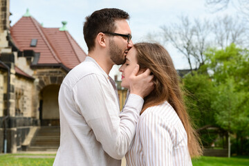 Naklejka premium Young man kissing his girlfriend on her forehead in park