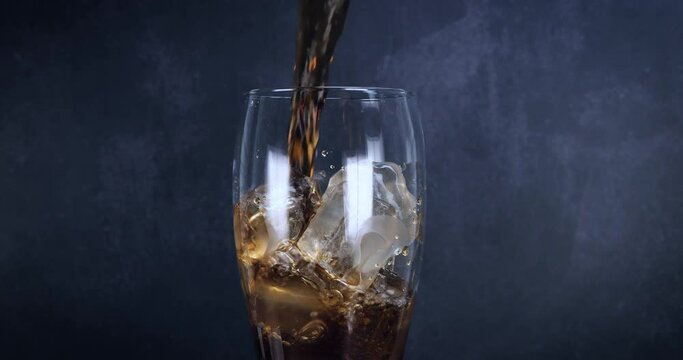 Cool glass of cola drink with ice, bubbles and fizz. Fresh cold sweet drink poured over ice cubes. Cola glass with summer refreshment on black. Slow motion 4k