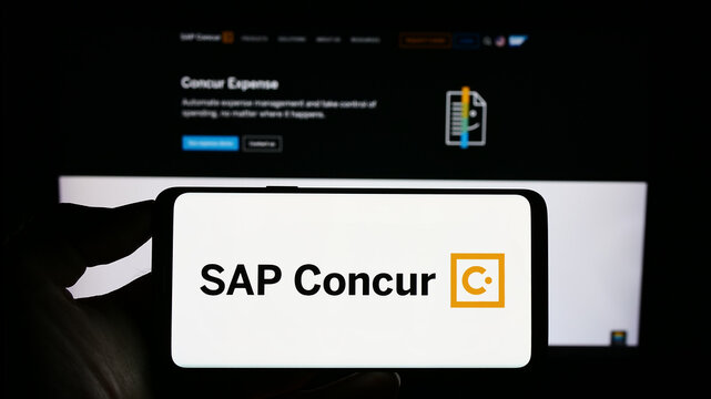 Stuttgart, Germany - 07-11-2023: Person holding cellphone with logo of expense management software SAP Concur on screen in front of business webpage. Focus on phone display.
