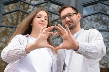 Beautiful happy couple making heart shape with their hands in city