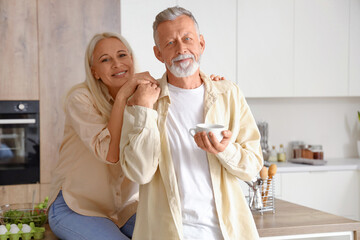 Fototapeta na wymiar Mature man with cup of coffee and his wife in kitchen