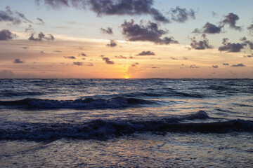 lever de soleil color&eacute; au dessus de l'horizon avec des petits nuages dans le ciel au dessus de l'oc&eacute;an avec des vagues