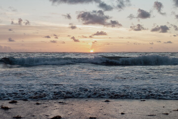 lever de soleil avec des petits nuages dans le ciel au dessus de l'océan avec des vagues tel que vu à partir de la plage