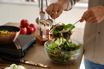 Mature man making vegetable salad in kitchen, closeup