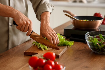 Mature man cutting lettuce in kitchen, closeup