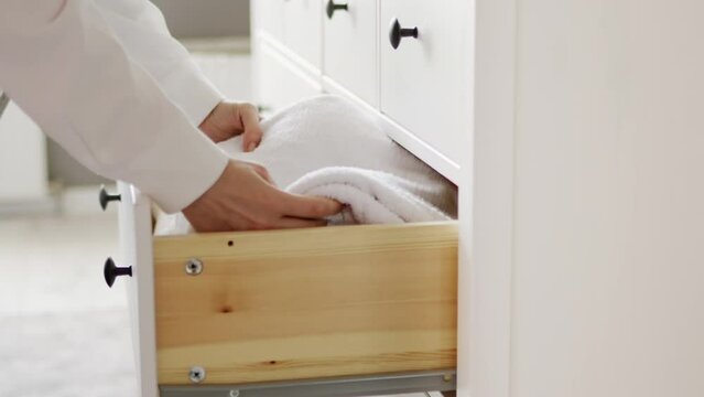 A housewife folds clean bedding or white towels after washing into a laundry box in a chest of drawers. Organization and storage of home comfort in the house