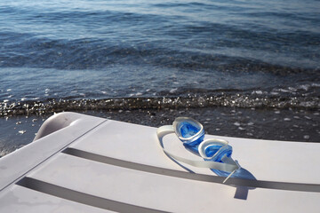 Swimming goggles by the sea. Summer vacation concept background. Focused on the blue goggles.      ...