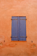 Obraz premium Closed vintage window of blue colour with old wooden shutters on the vibrant orange wall. Elegant retro architectural details