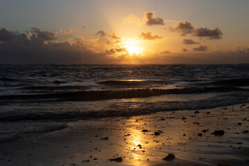 Fototapeta na wymiar Vue de l'océan mouvementé lors d'un lever de soleil aux lueurs jaunes à partir de la plage