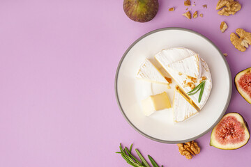Plate with pieces of tasty Camembert cheese on lilac background