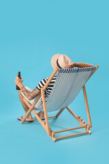 Young man with beer sitting in deck chair on blue background, back view