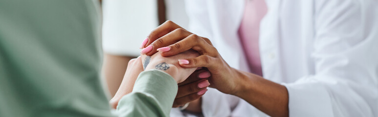 partial view of african american woman holding hands of tattooed female friend while supporting and...
