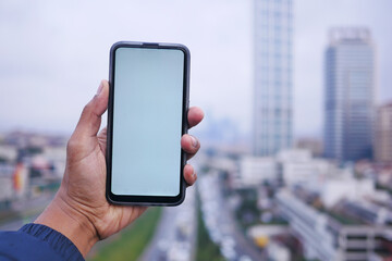 young man hand using smart phone with green screen against city buildings 