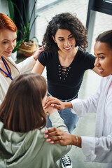 high angle view of diverse group of pleased multicultural women joining hands near positive...