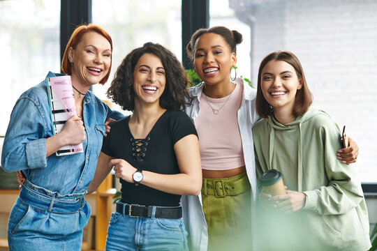 diverse group of stylish and excited multiethnic female friends with coffee to go, smartphone and magazine looking at camera and laughing in women club, mutual support, solidarity and trust concept