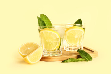 Fototapeta premium Wooden board with glasses of cold mojito, lemon and mint on color background