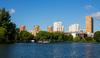 Fototapeta na wymiar Beautiful panoramic landscape - modern high-rise buildings on the shore of a pond among the lush foliage of trees in Reutov, Moscow region on a clear summer sunny day