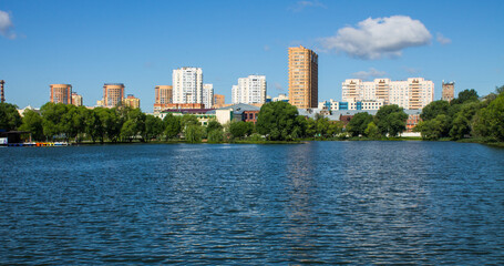 Beautiful panoramic landscape - modern high-rise buildings on the shore of a pond among the lush foliage of trees in Reutov, Moscow region on a clear summer sunny day