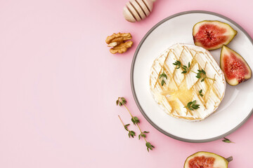 Plate of tasty baked Camembert cheese on pink background