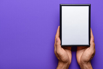 Man holding blank photo frame on purple background