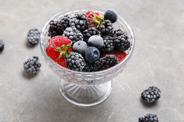 Glass bowl of frozen berries on grey grunge background