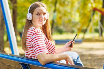 A woman wearing headphones listening to music while sitting on a bench