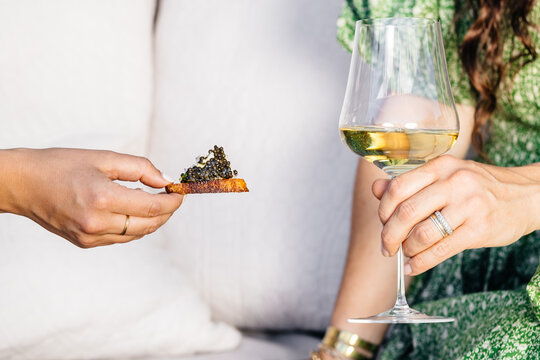 Female hands holding caviar and white wine in styled composition 