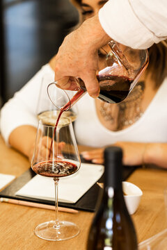 Hand pouring red wine into a glass for another person at a winery