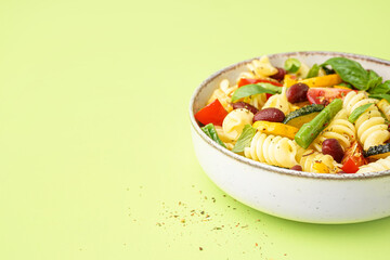 Bowl of tasty pasta salad with tomatoes and basil on green background